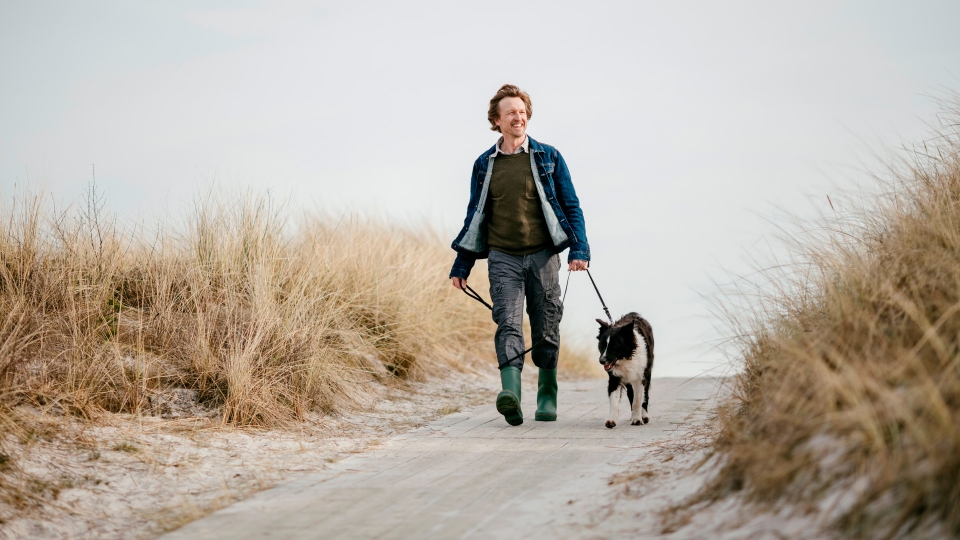 Man wandelt met hond over het duinpad.