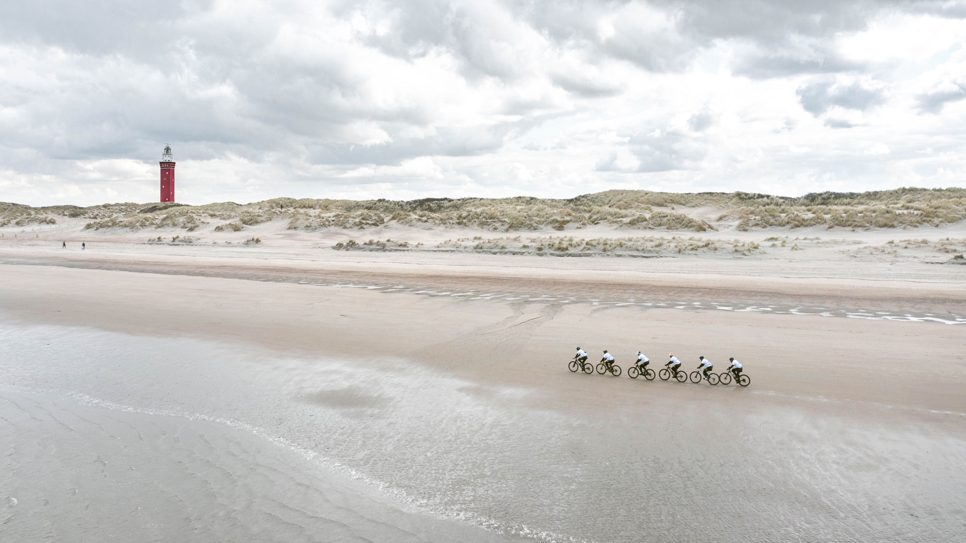 Fietsers op het strand bij Ouddorp met vuurtoren op de achtergrond